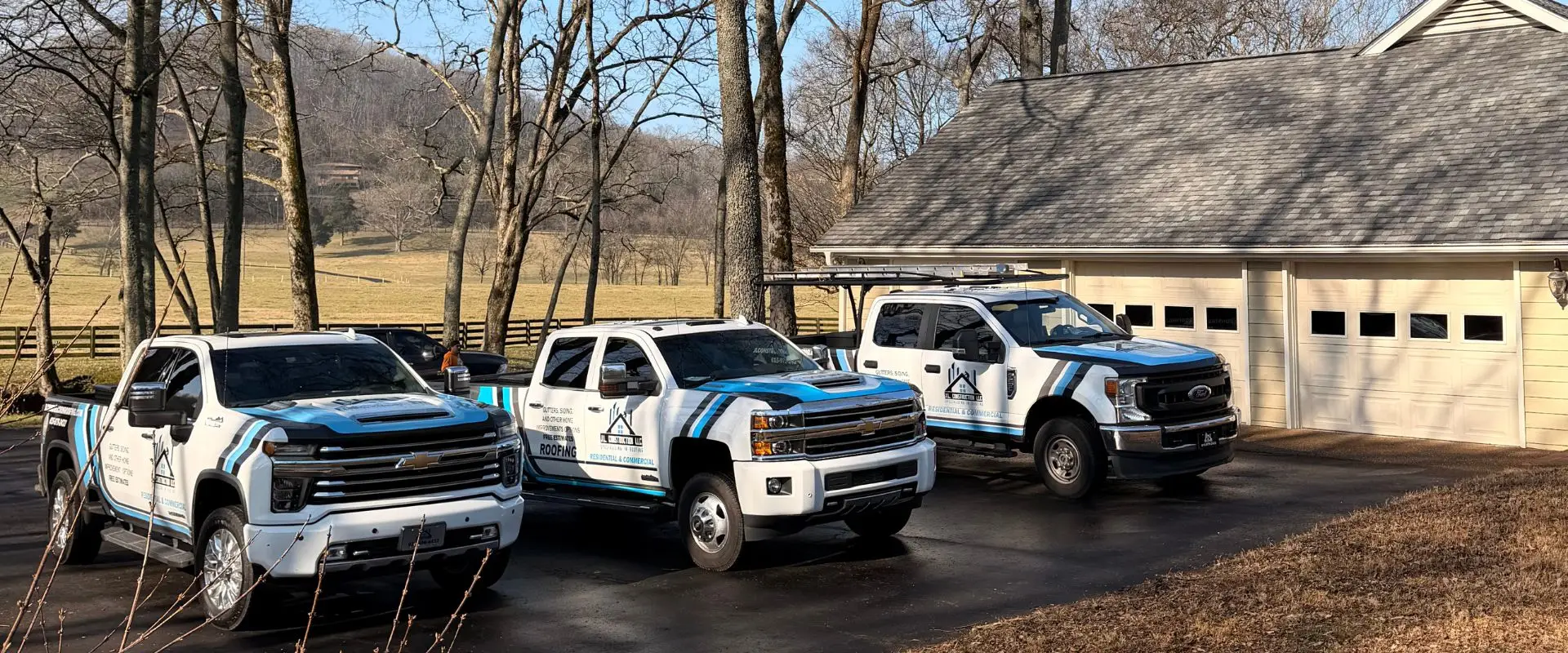 Three J.L. Construction LLC service trucks with matching white, blue, and black branding parked in a row on a paved driveway in front of a residential garage.